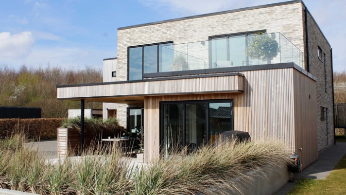 Materialerne komplimenterer hinanden på fornem vis. Se bare de lyse farver i træet og murværket, som brydes af de sorte vinduesrammer og nedløbsrør. .